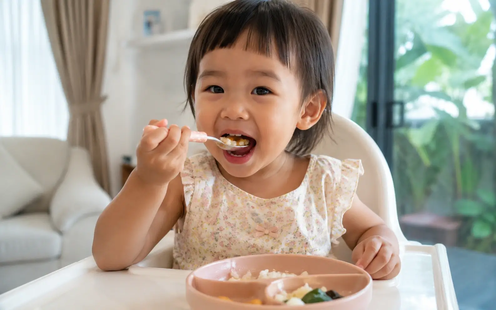 เด็กไทยวัยประมาณ 2-3 ปี กำลังกินอาหารอย่างมีความสุขในบ้าน สีหน้าสบาย
